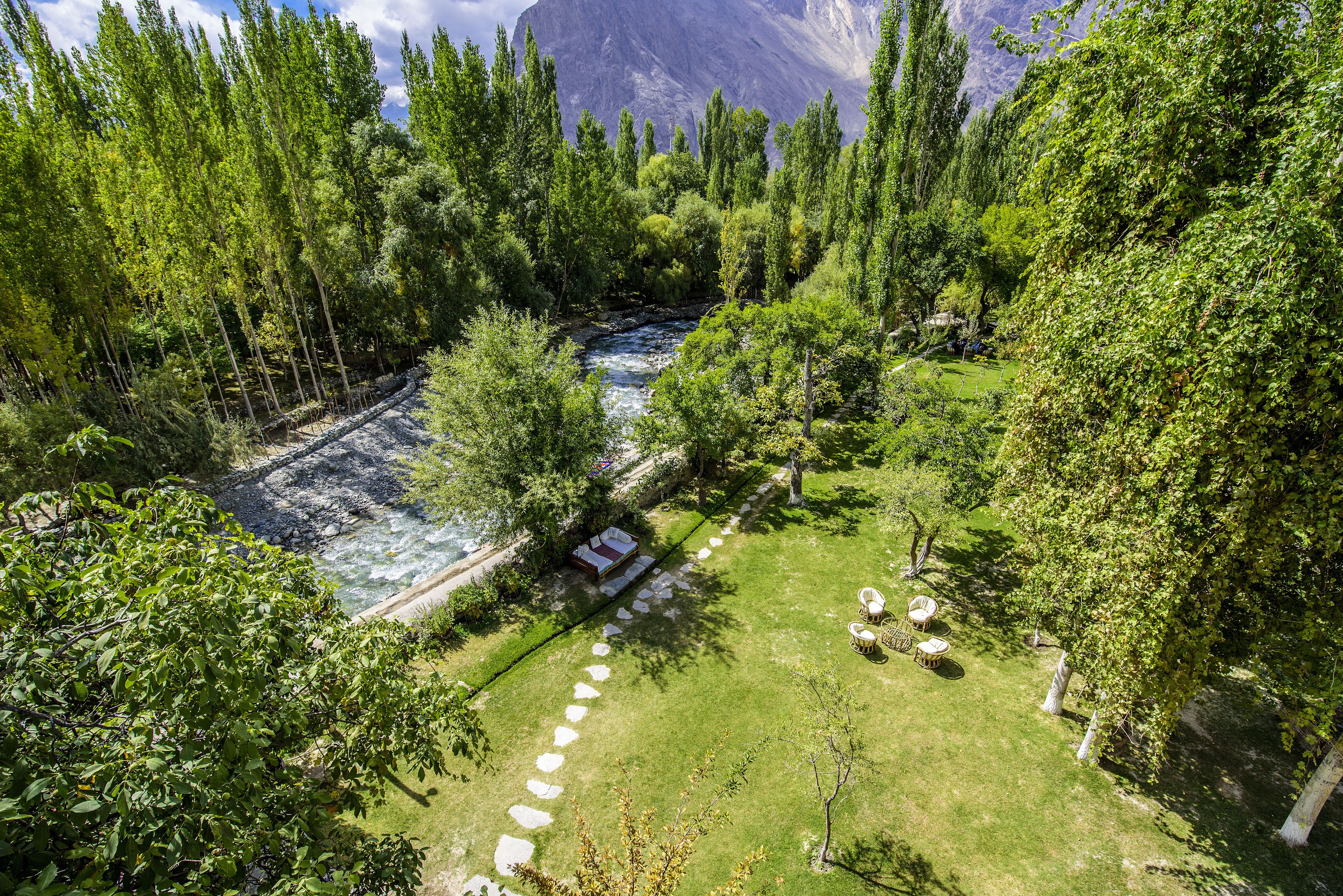 A lush garden with a river, a small building, and a clear view of a mountain range.