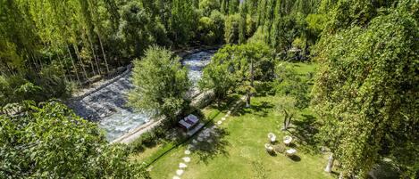 A lush garden with a river, a small building, and a clear view of a mountain range.