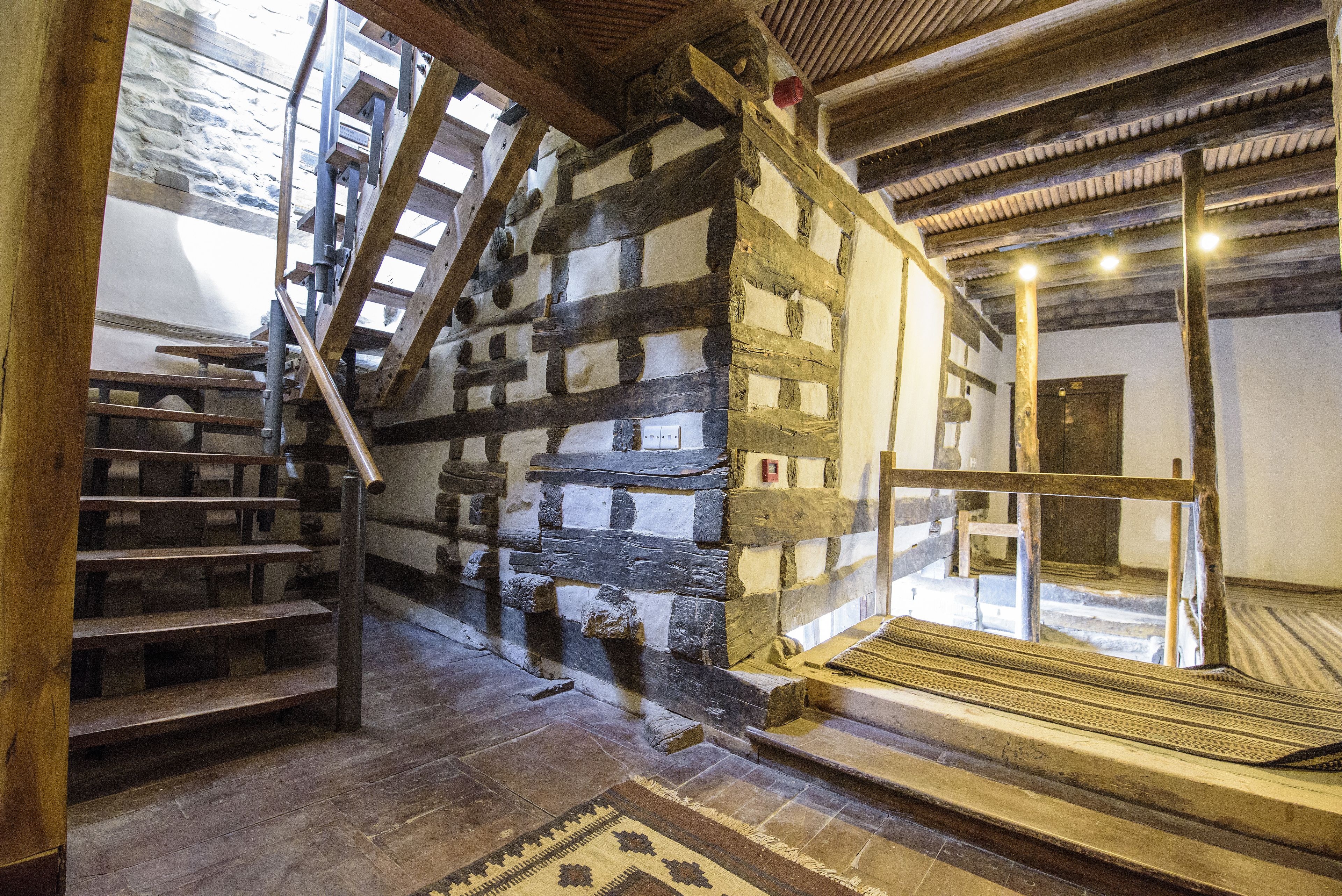 Un escalier en bois, un mur en pierre, un plancher en bois et un tapis à motifs.