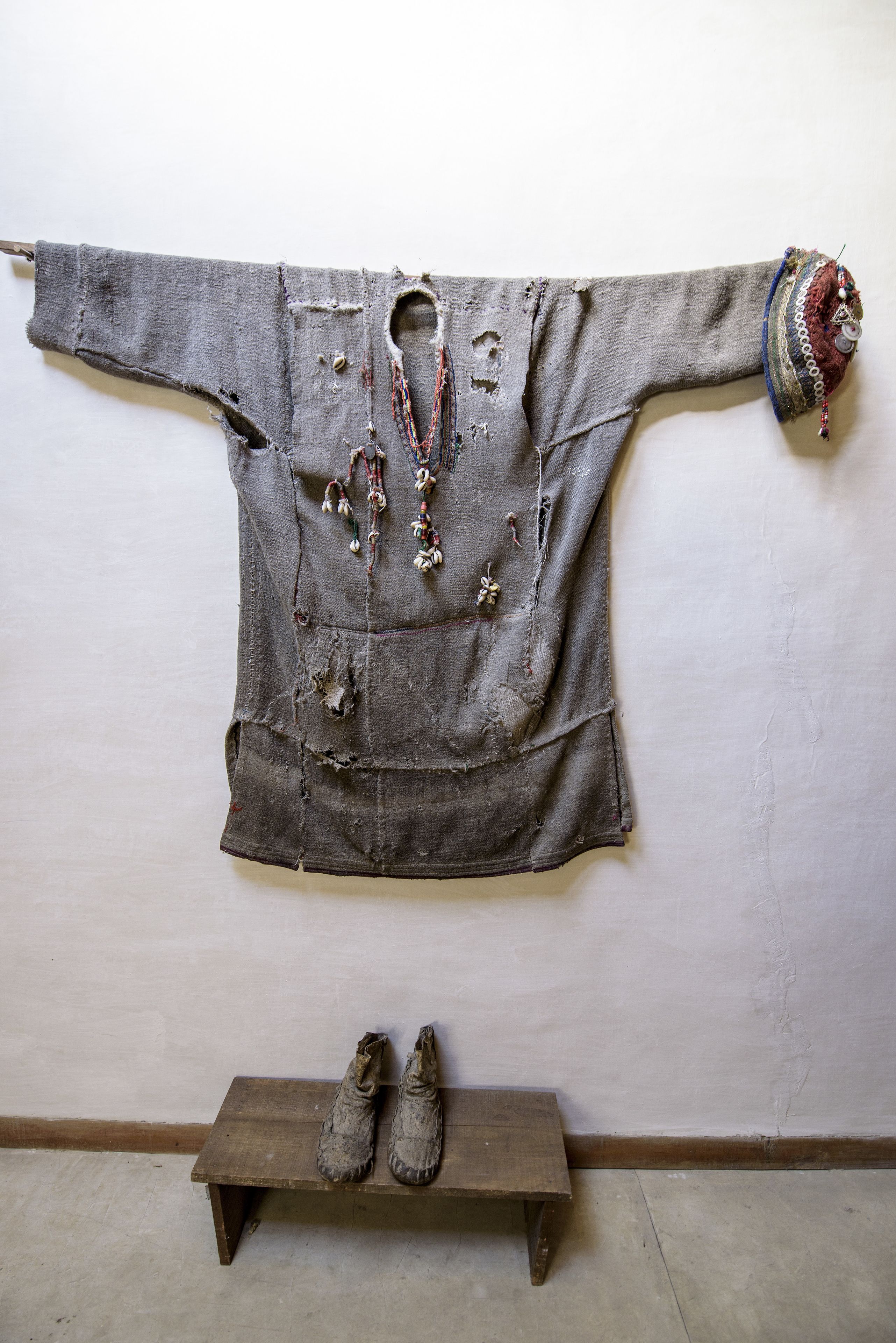 A room with a wooden bench, a pair of shoes, and a wall-mounted piece of clothing with decorative elements.