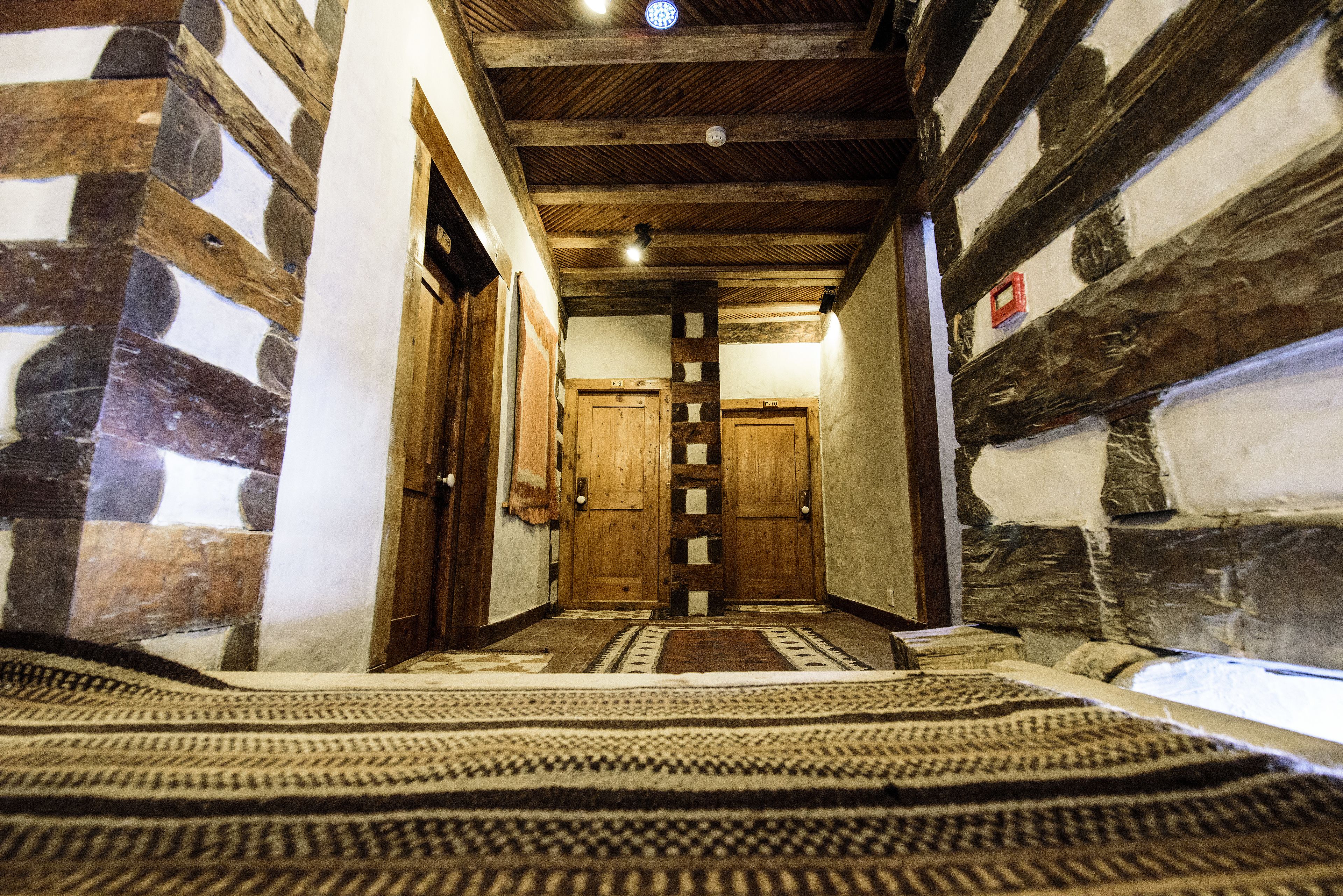 A hallway with wooden beams and stone walls, leading to two wooden doors.