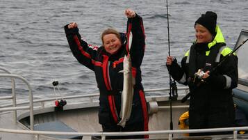 Two people on a boat holding a fish, with a railing and water in the background.