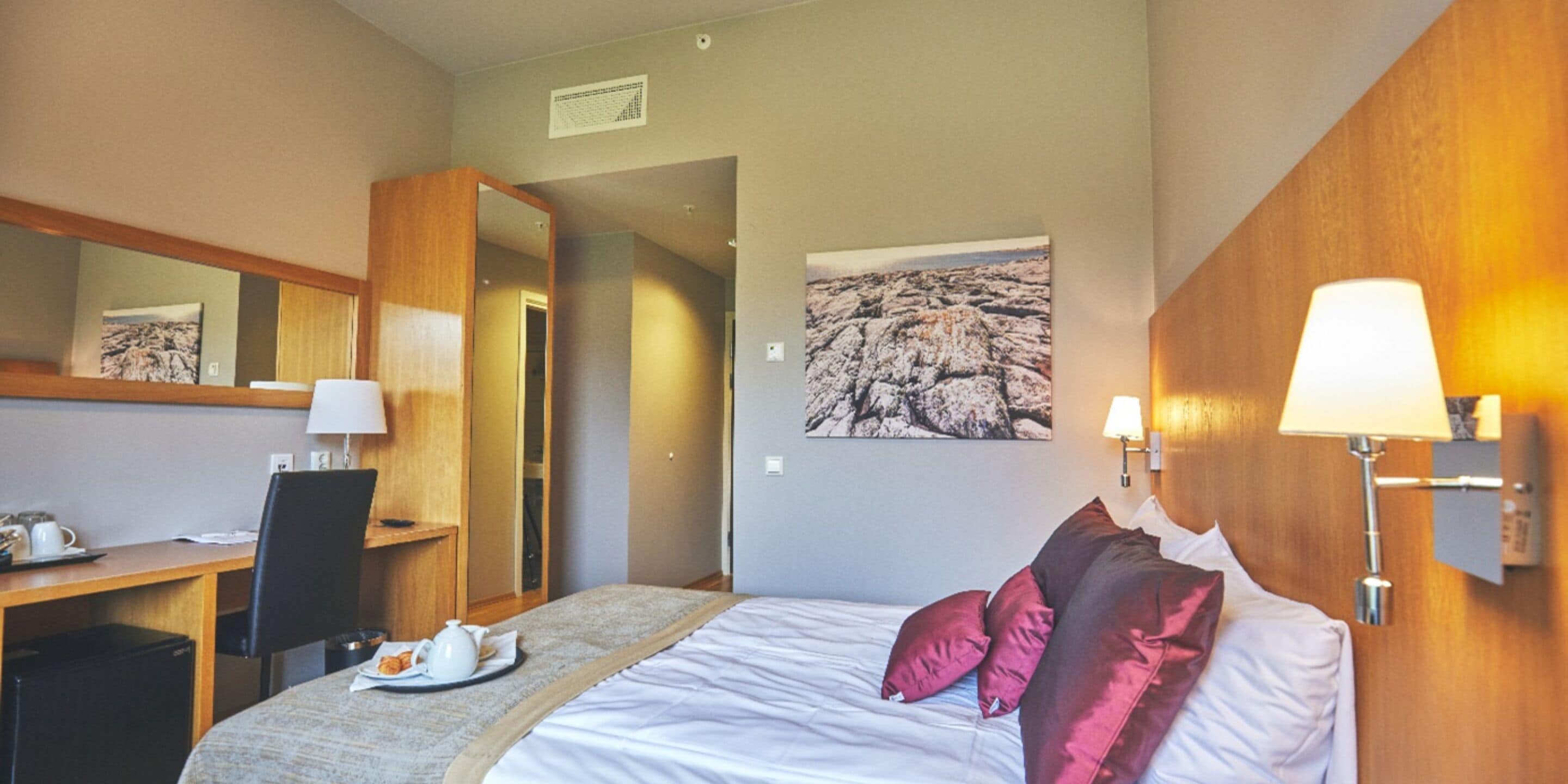 Una camera d'albergo con un letto, una scrivania con una sedia, una lampada e un quadro appeso al muro.