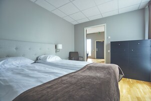 Una habitación de hotel con cama, una silla, un armario y una puerta que da a otra habitación.