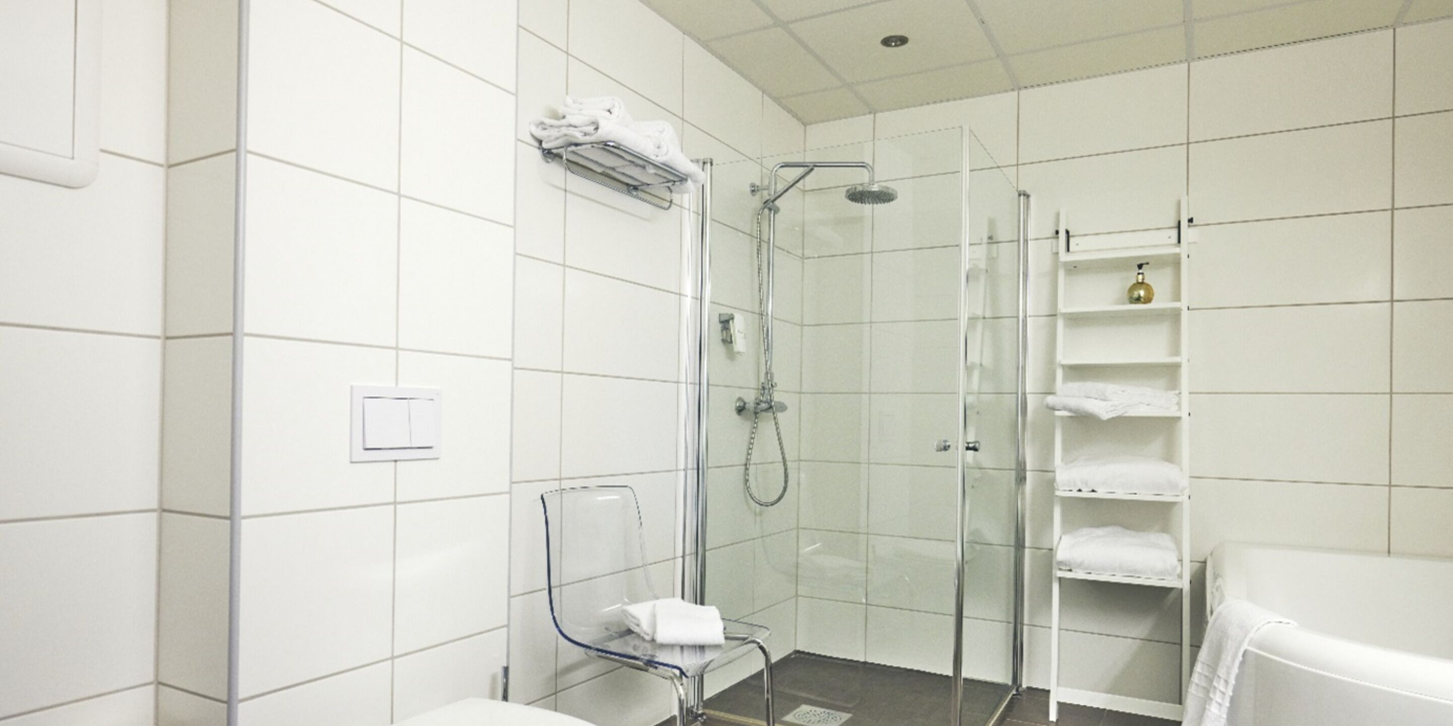 A modern bathroom with white tiles, a glass shower enclosure, a glass shower chair, and a white toilet.