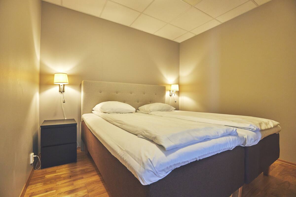 A neatly made bed with white linens in a room with wooden flooring and two bedside lamps.