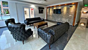 A modern lobby with a black leather sofa, a tufted armchair, and a wooden coffee table. - Lotus Hotel (Silifke)