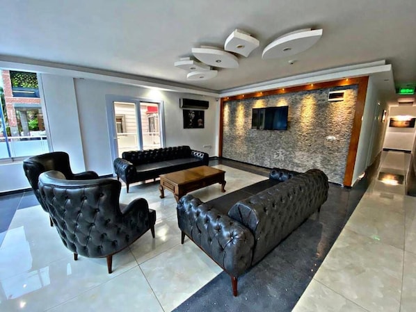 A modern lobby with a black leather sofa, a tufted armchair, and a wooden coffee table. - Lotus Hotel (Silifke)