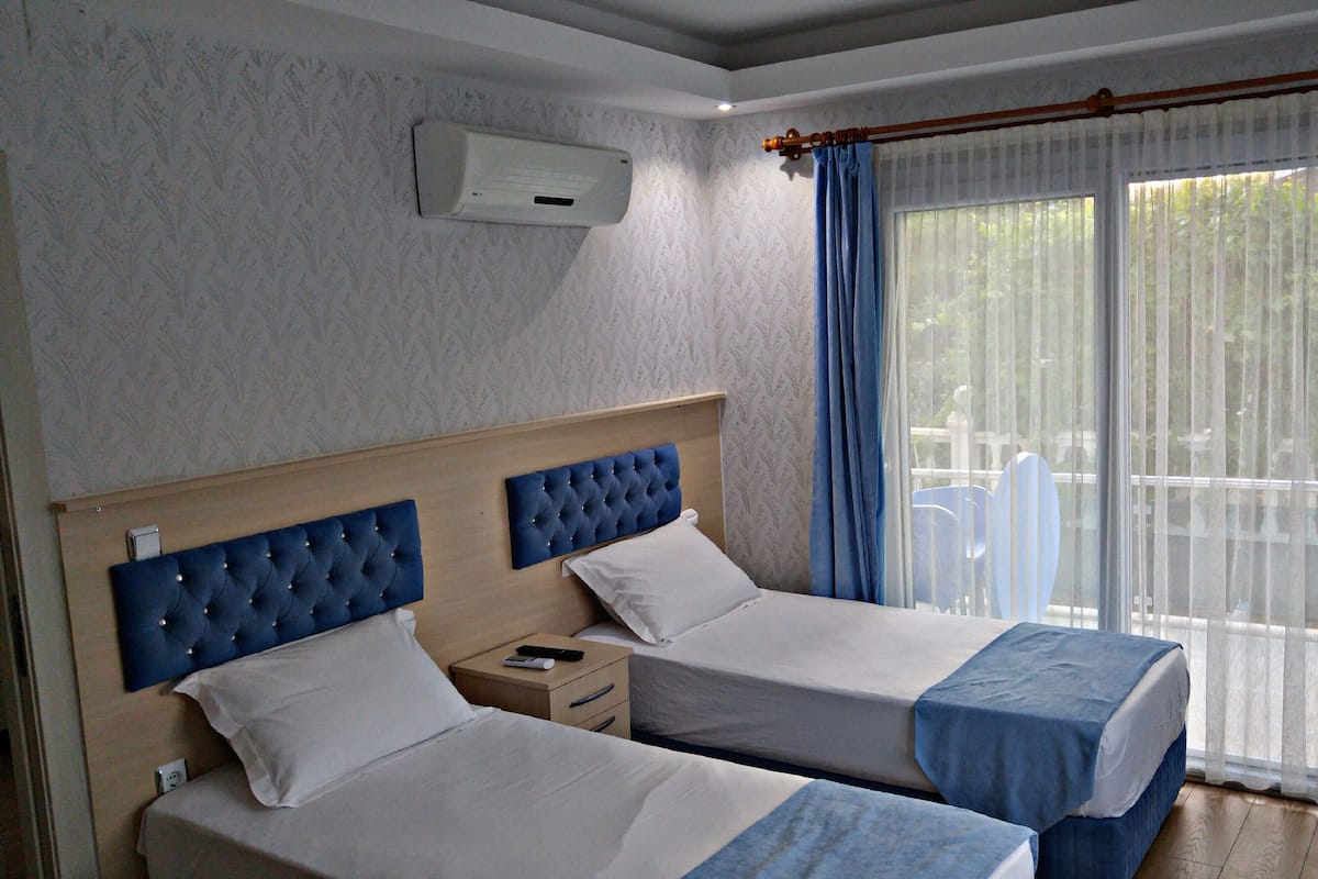 A hotel room with two beds, a TV, and a balcony with blue curtains.