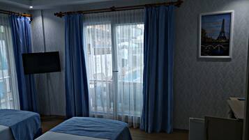Ein Hotelzimmer mit zwei Betten, einem Fernseher und einem Balkon mit blauen Vorhängen.