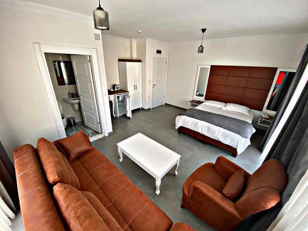 Una habitación de hotel moderna con una cama grande, un sofá, una mesita de centro y un baño visible a través de una puerta abierta.