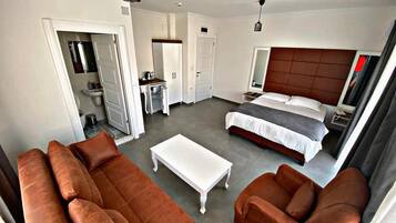 Una habitación de hotel moderna con una cama grande, un sofá, una mesita de centro y un baño visible a través de una puerta abierta.