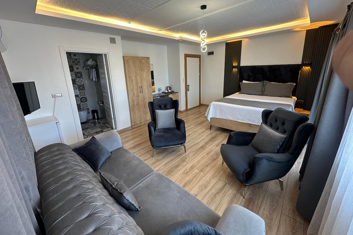 A modern hotel room with a sofa, armchairs, a bed, and a TV.