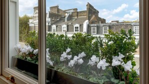 A window with white flowers and a view of a historic building with multiple chimneys and a white fence. - Luxury Notting Hill 3 bedroom, 2 Bathroom Duplex Apartment (London)