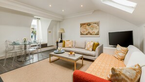 A modern living room with a glass dining table, a sofa, a television, and a skylight. - Luxury Notting Hill 3 bedroom, 2 Bathroom Duplex Apartment (London)