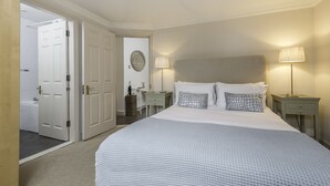 A bedroom with a large bed, two bedside tables with lamps, a dresser, and a door leading to a bathroom. - Luxury Notting Hill 3 bedroom, 2 Bathroom Duplex Apartment (London)