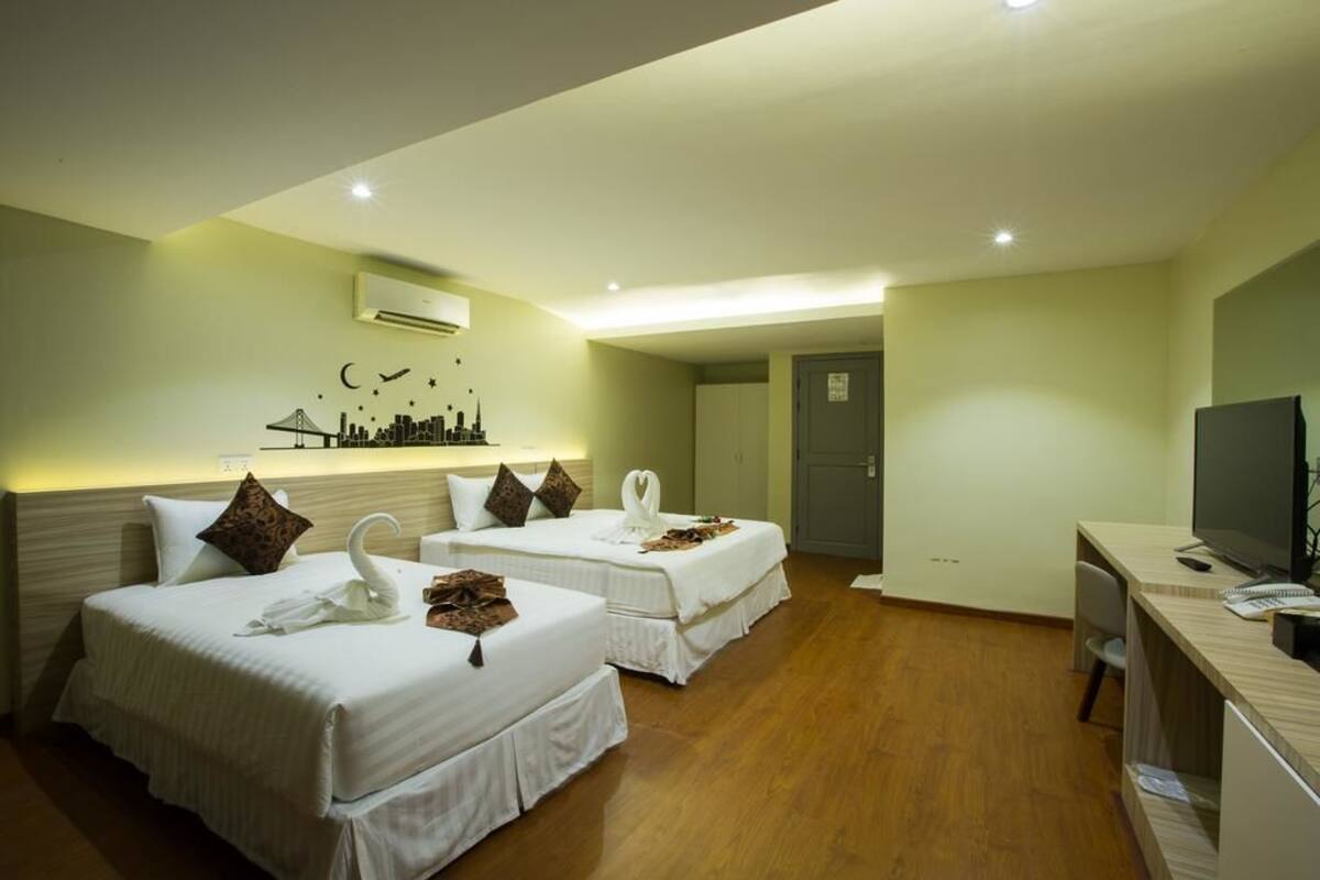 A hotel room with two beds, a desk, a TV, and a cityscape artwork on the wall.