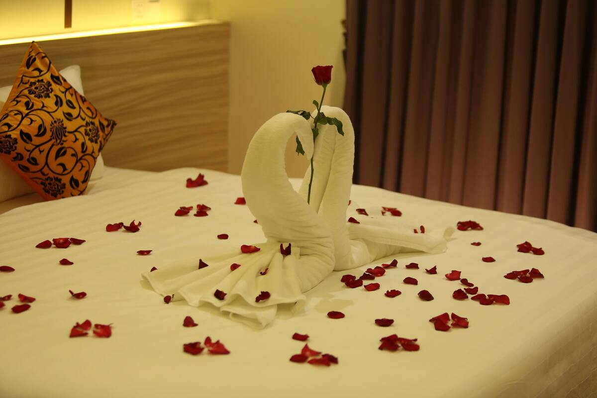 A bed with a swan-shaped centerpiece made of white fabric and a single red rose, surrounded by scattered rose petals.