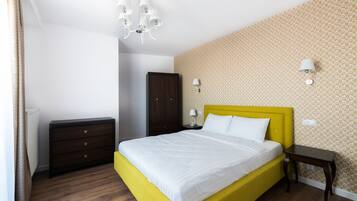 A bedroom with a yellow bed, wooden dresser, and patterned wallpaper.