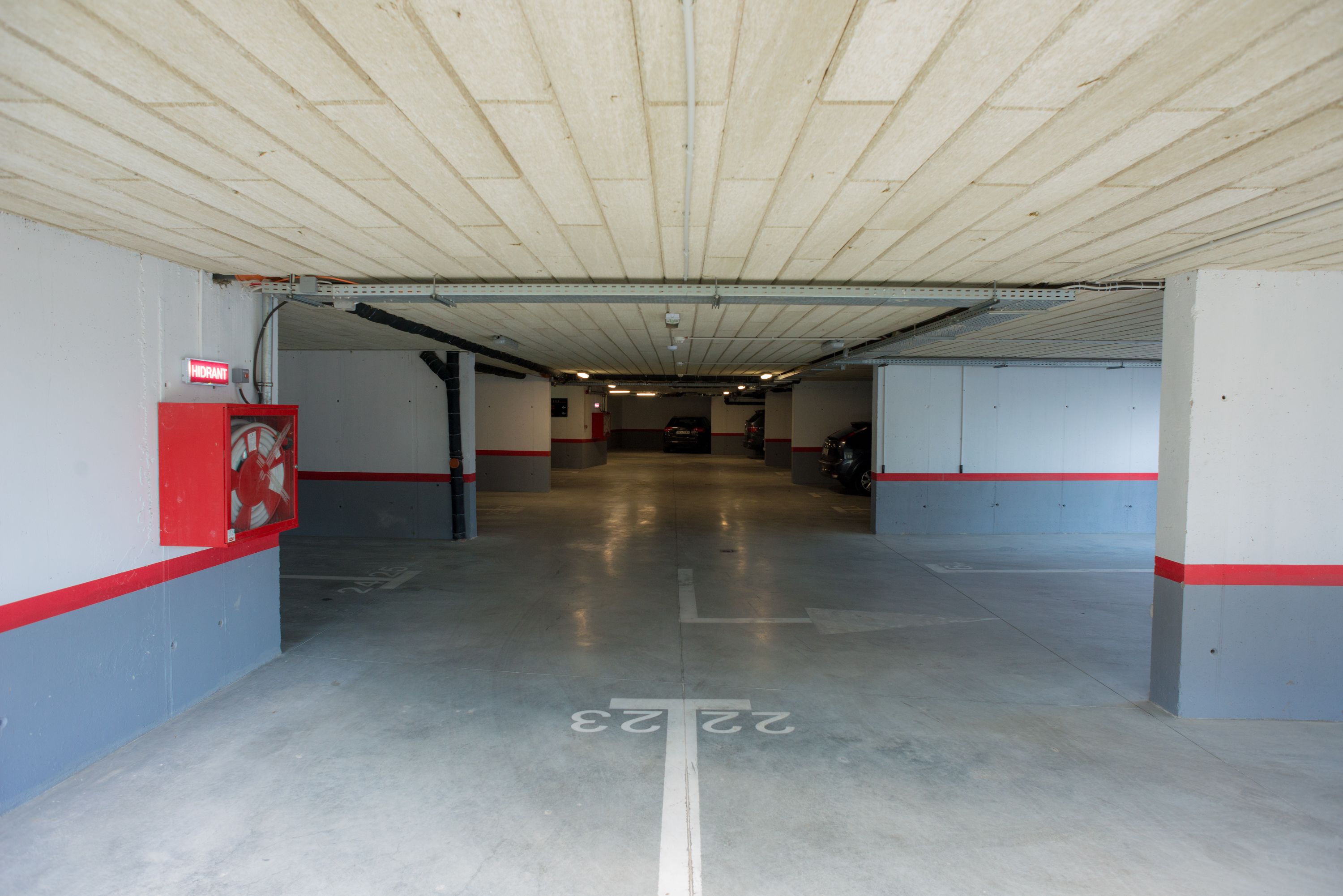Un garaje de estacionamiento con un camino despejado señalado por números en el piso, un hidrante y un cuadro rojo de emergencia.