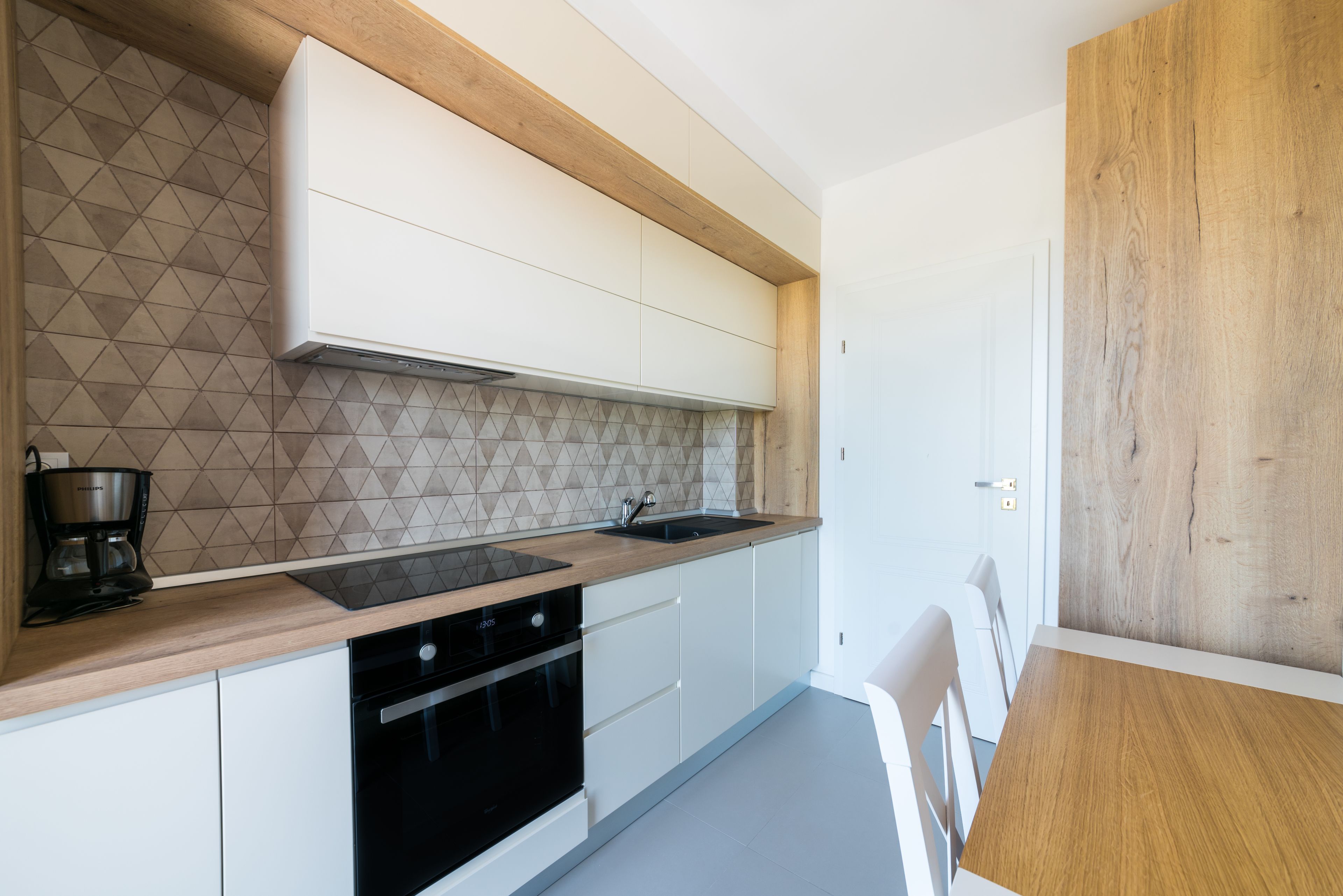A modern kitchen with white cabinets, a black stove, and a wooden countertop.