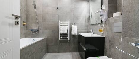 Un baño moderno con bañera, inodoro y lavamanos, con azulejos grises y un perchero para toallas.