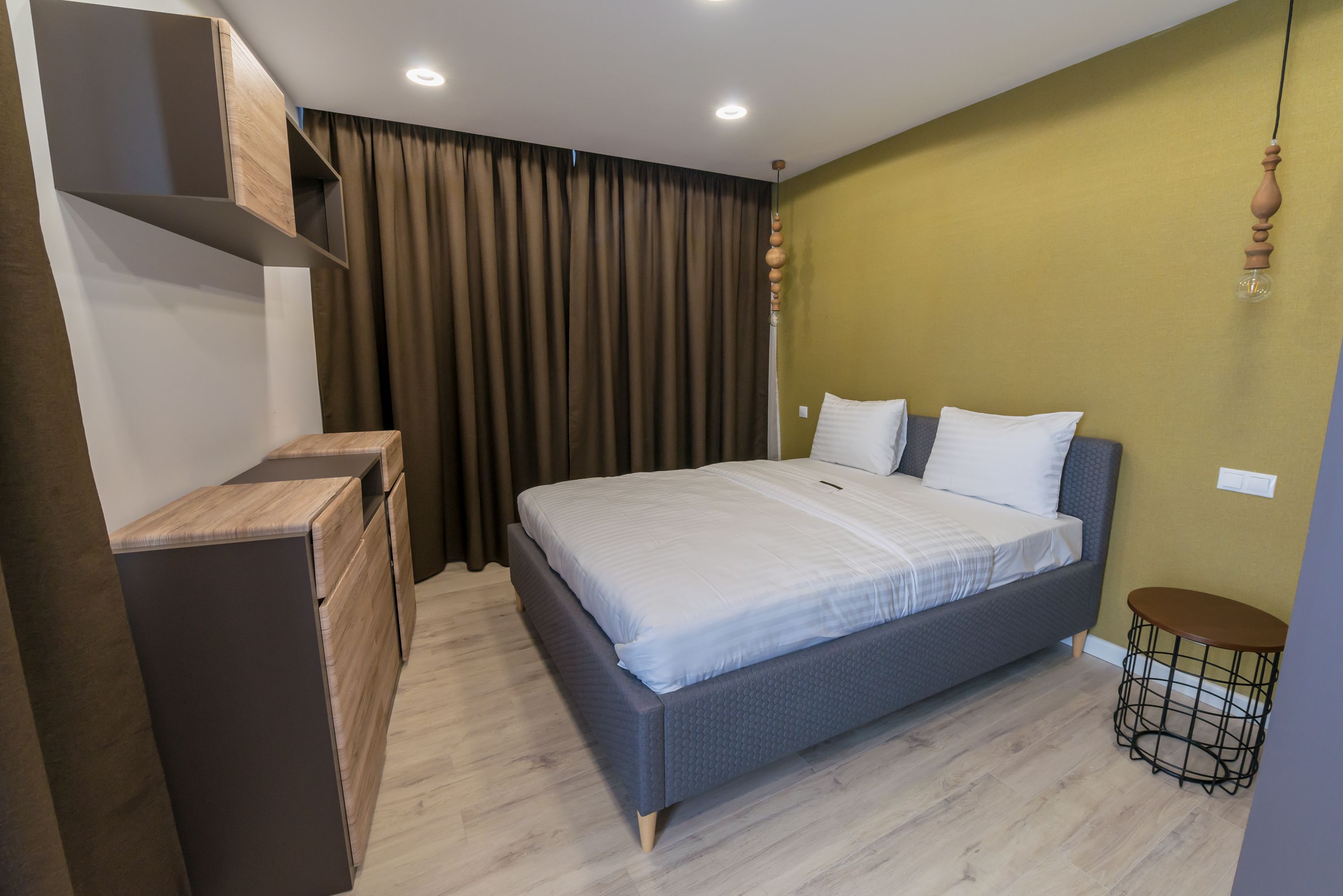 A modern bedroom with a bed, a dresser, a small table, and a hanging light fixture.