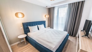 A modern hotel room with a large bed, two bedside tables, a TV, and a window with curtains. - UBA Accommodation (Cluj-Napoca)