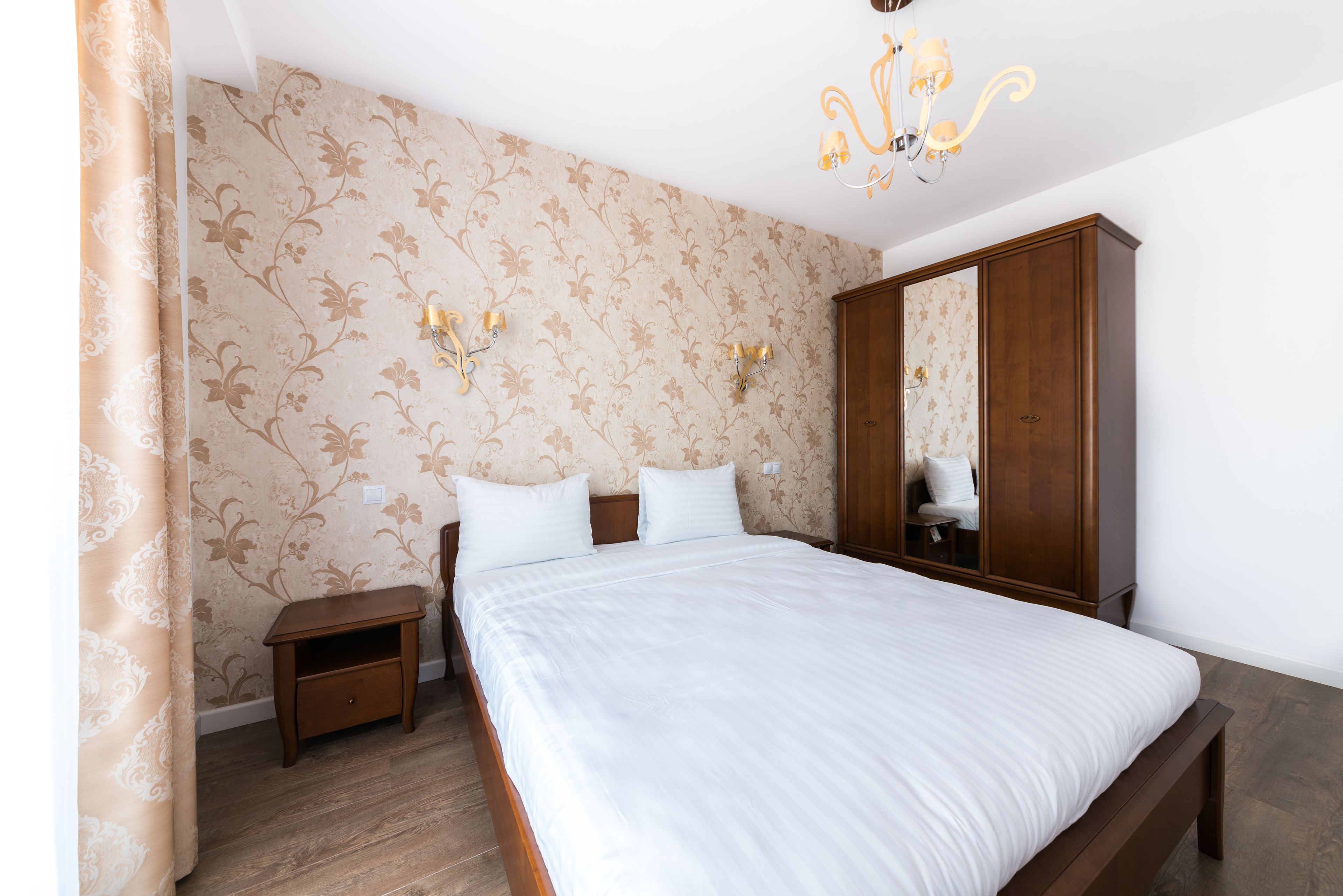 A bedroom with a large bed, wooden nightstand, and a wardrobe.