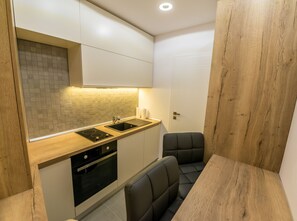 A compact kitchen with a built-in oven, a double sink, and a seating area with a wooden table.