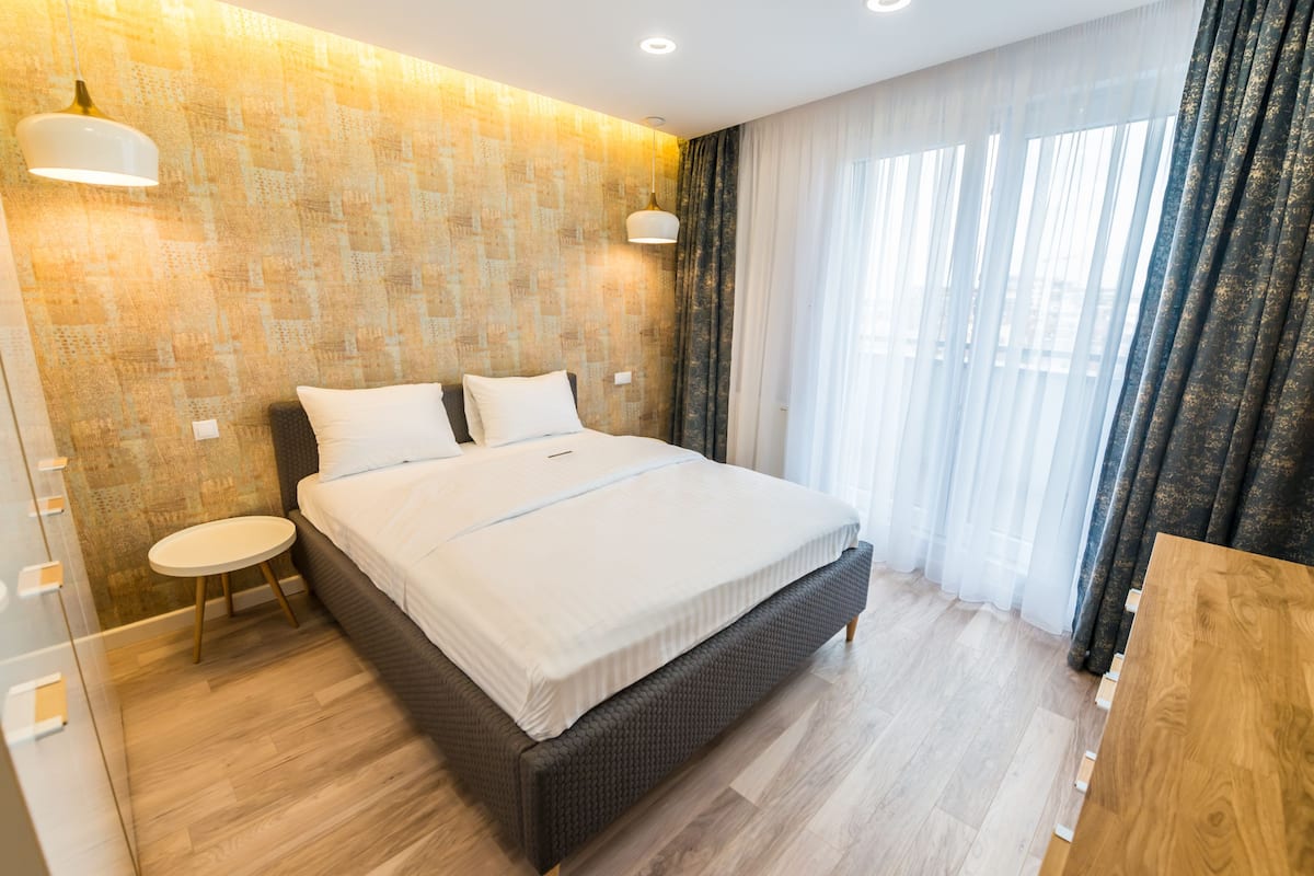 A modern hotel room with a large bed, a small round table, and a wooden nightstand.
