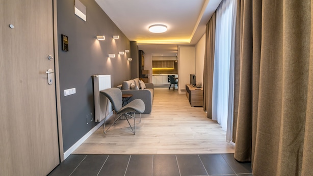 A modern hotel hallway with a sofa, a small table, and a kitchen area in the background. - UBA Accommodation (Cluj-Napoca)