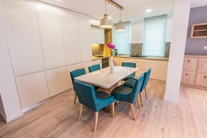 A modern kitchen with white cabinets, a wooden countertop, and a dining area with a white table and teal chairs.