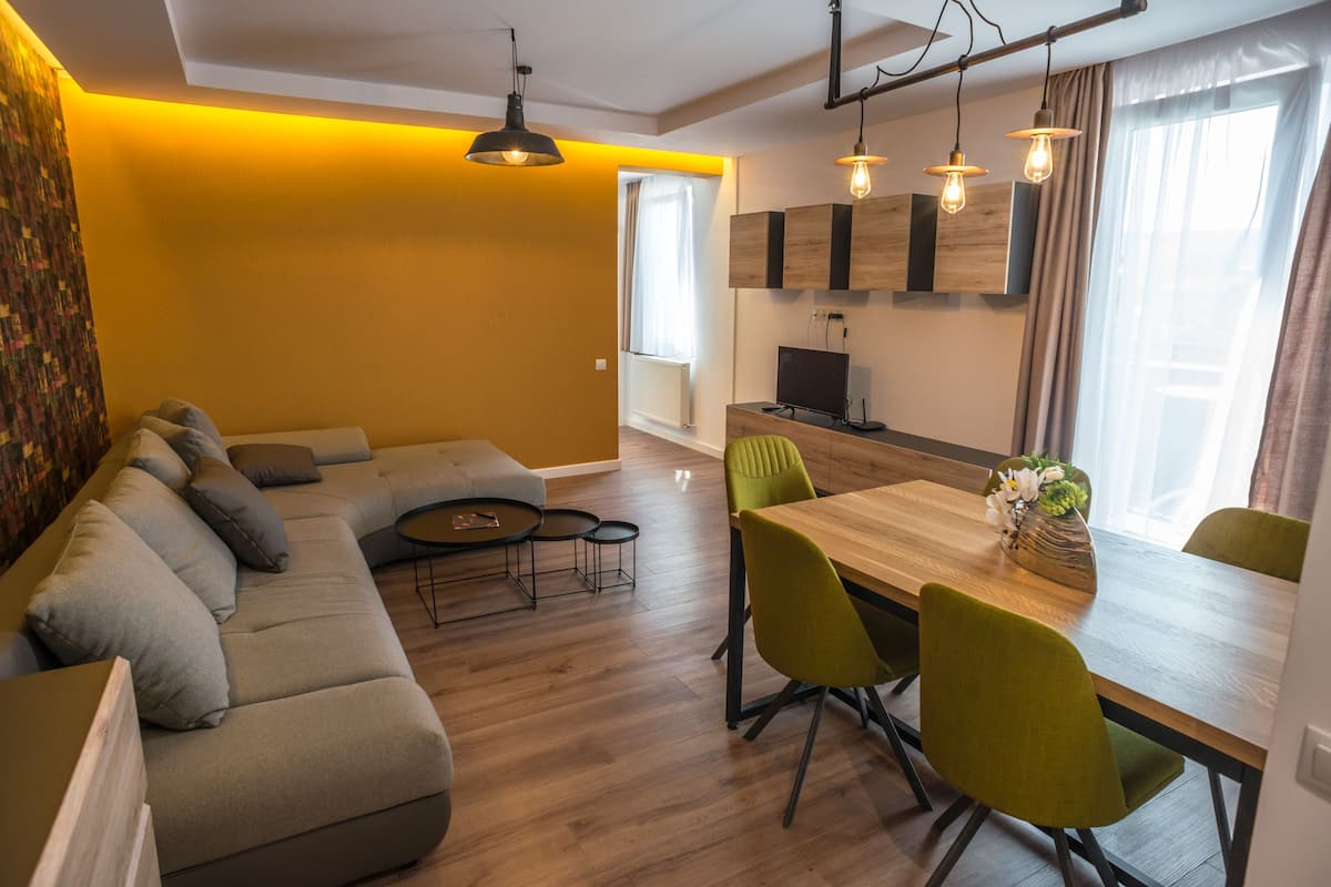 A modern living room with a sofa, dining table, and chairs. There is a television and a small table with a lamp.