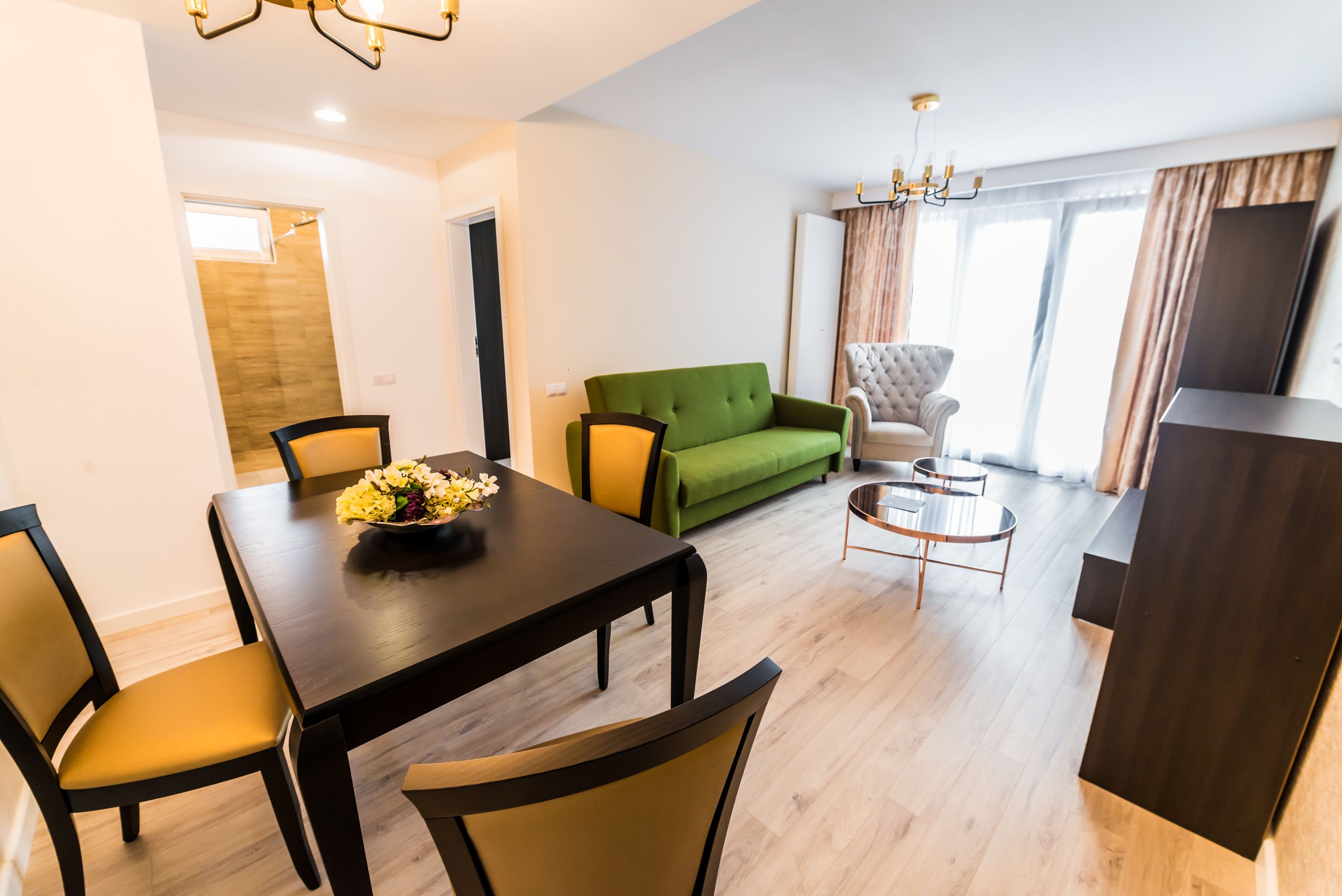 Una sala de estar moderna con comedor, un sofá verde, un sillón capitoné y un mueble para televisor.