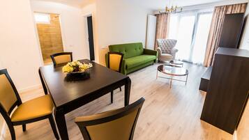 Una sala de estar moderna con comedor, un sofá verde, un sillón capitoné y un mueble para televisor.