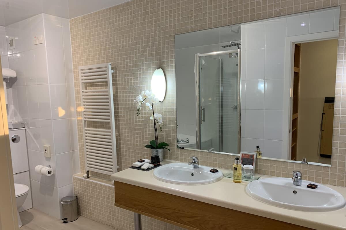 Uma casa de banho moderna com duas lavatórios, um espelho grande, um porta-toalhas e uma área de duche.