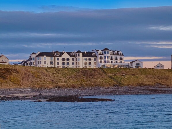 A coastal building with multiple floors, large windows, and a flat roof.
