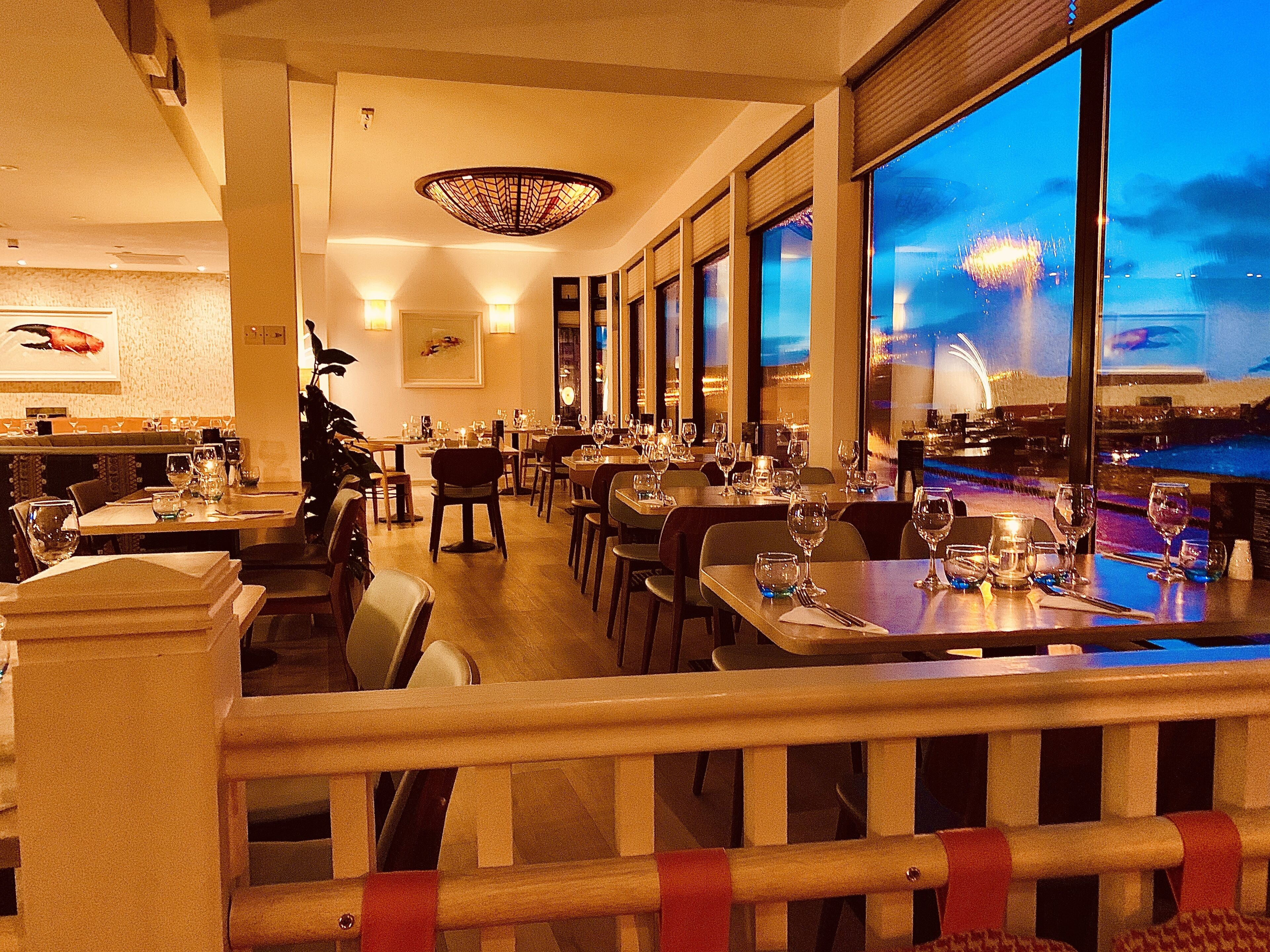 A restaurant with tables set for dining, a large window with a view of fireworks, and a decorative ceiling light.