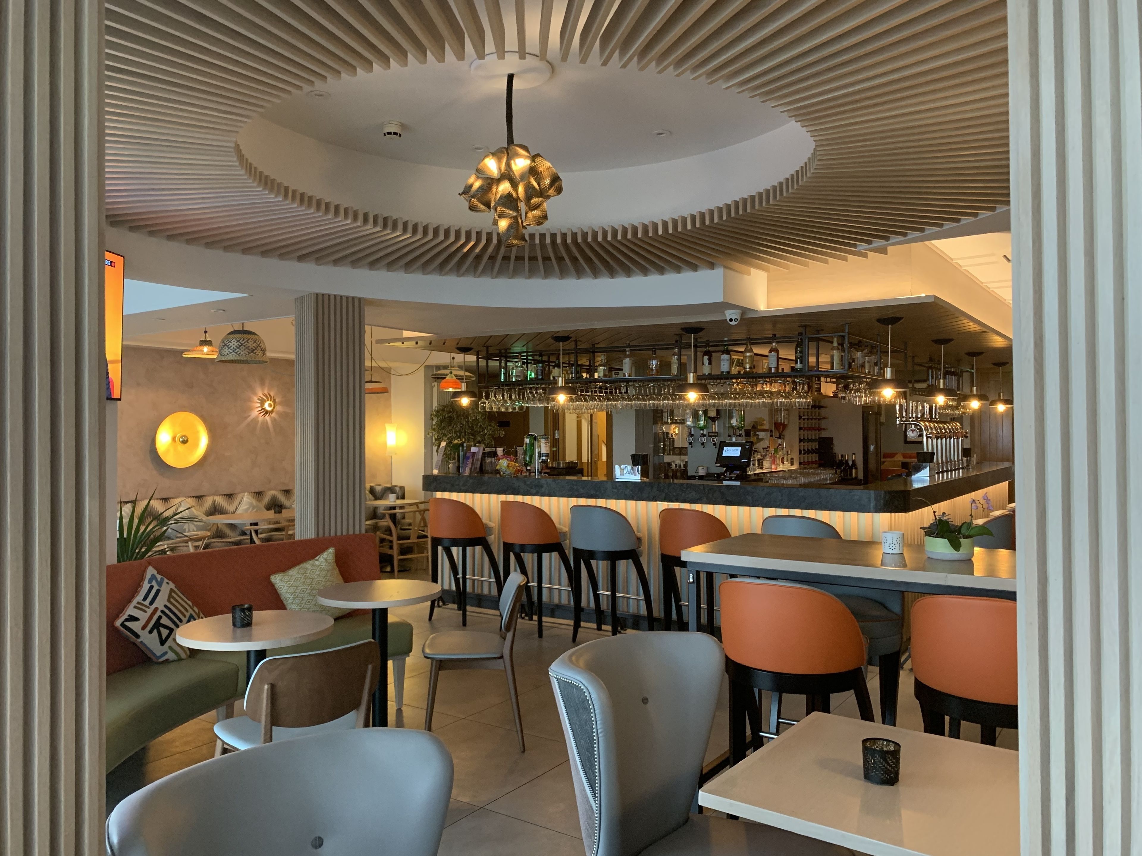 A modern bar area with a curved ceiling, bar stools, and a variety of bottles and glasses.