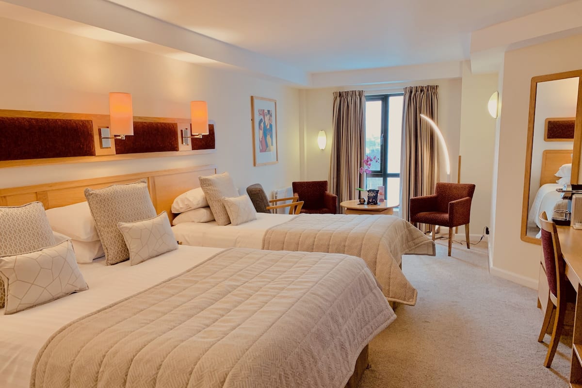 Quarto de hotel com duas camas, uma escrivaninha, uma cadeira e um espelho grande.