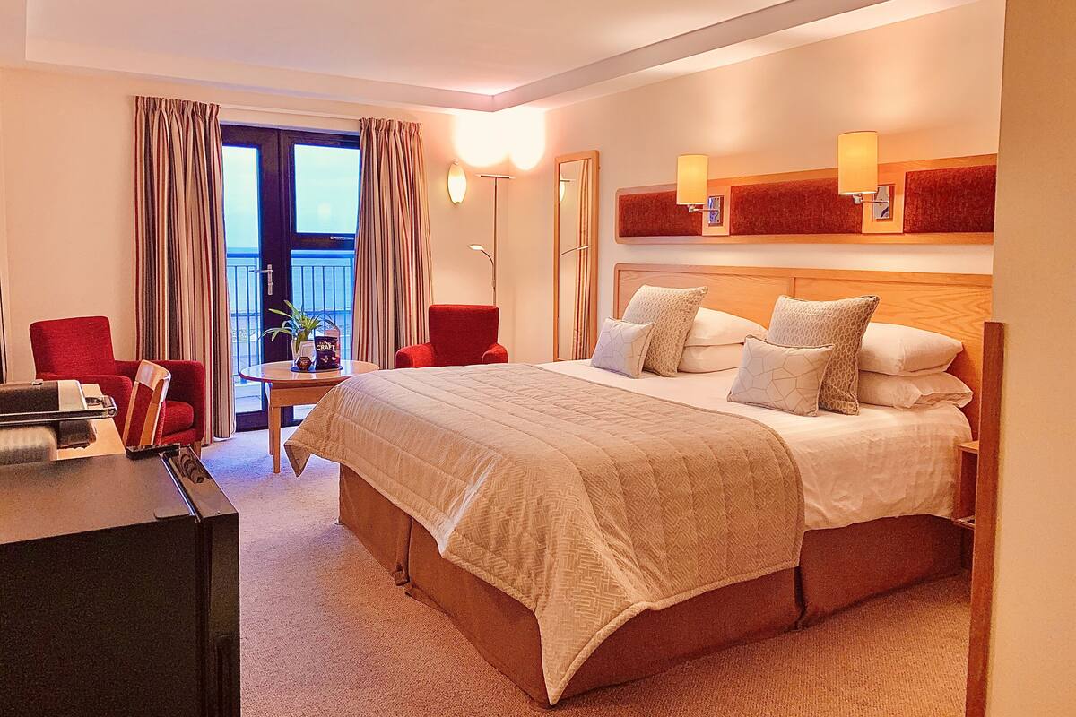 Quarto de hotel com uma cama grande, uma escrivaninha, uma cadeira e vista para o exterior.