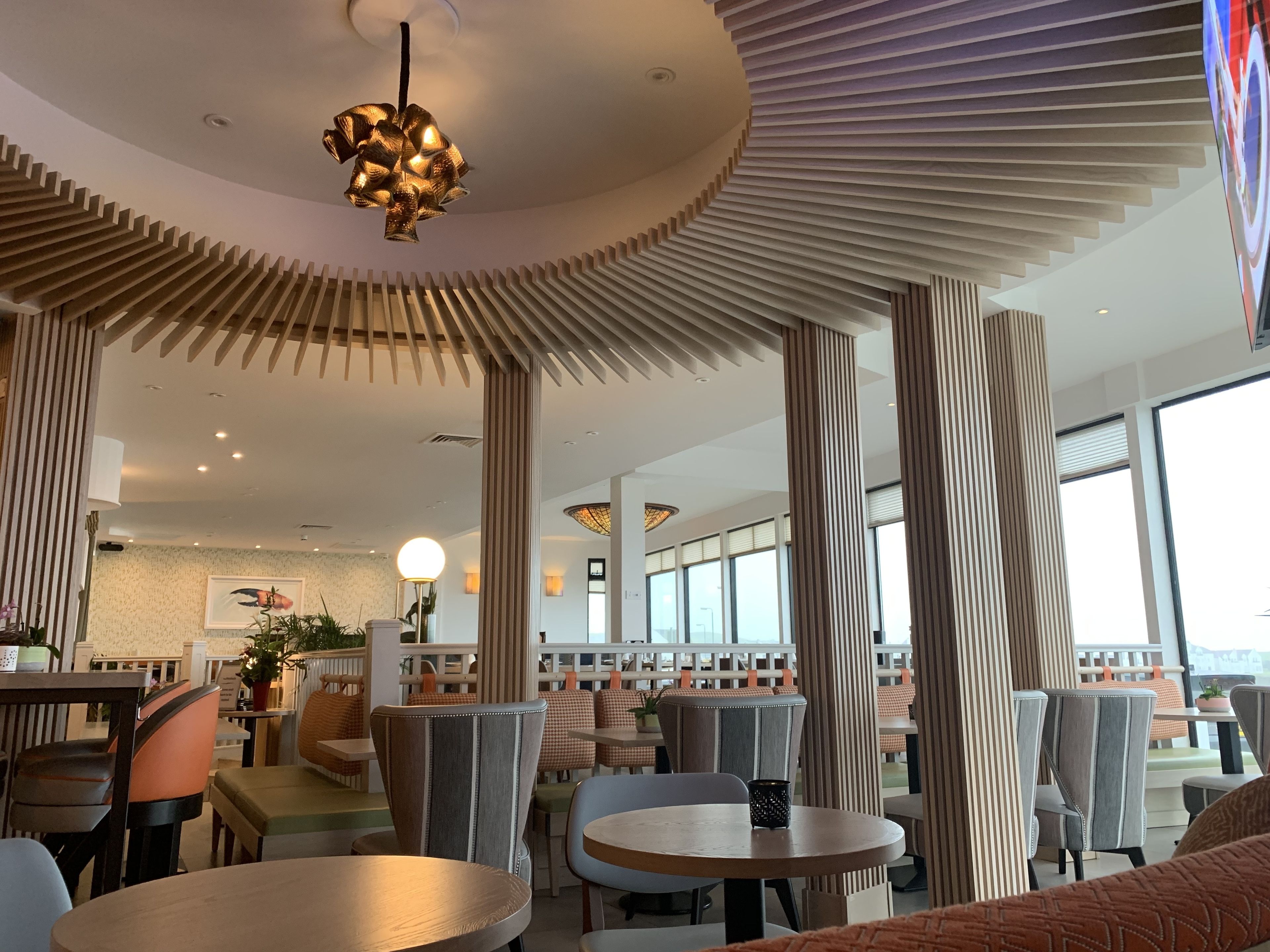 Ein modernes Restaurant mit runden Tischen, hohen Decken und vertikalen Holzleisten.