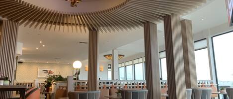 Ein modernes Restaurant mit runden Tischen, hohen Decken und vertikalen Holzleisten.