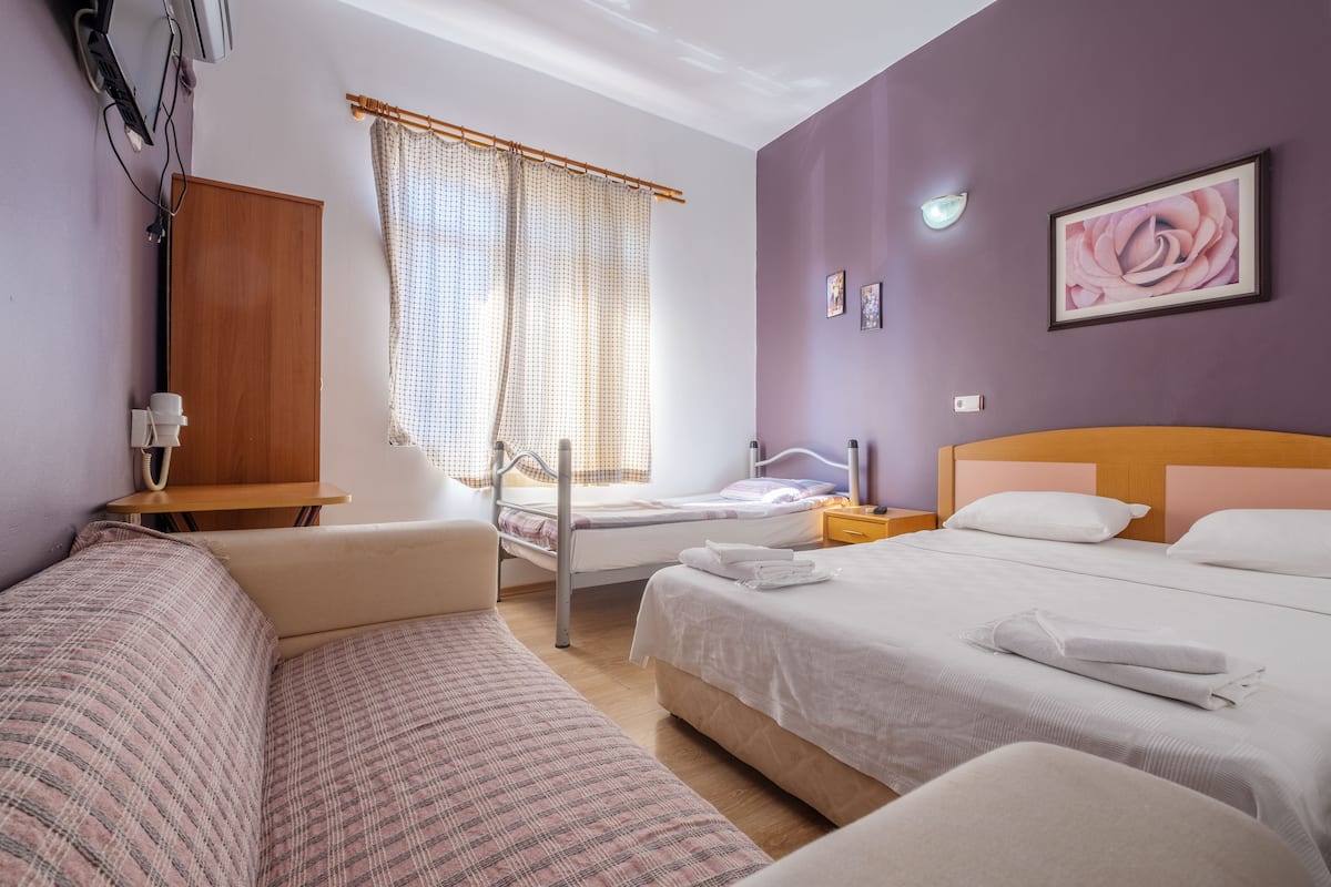 Une chambre d’hôtel comprenant un lit, un canapé, une table de chevet, une fenêtre avec des rideaux et un téléviseur fixé au mur.