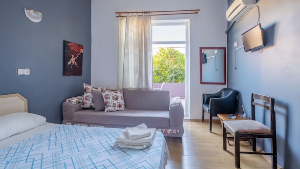 Ein Schlafzimmer mit Bett, Sofa, Sessel, Fernseher und einem Fenster mit Vorhängen.
