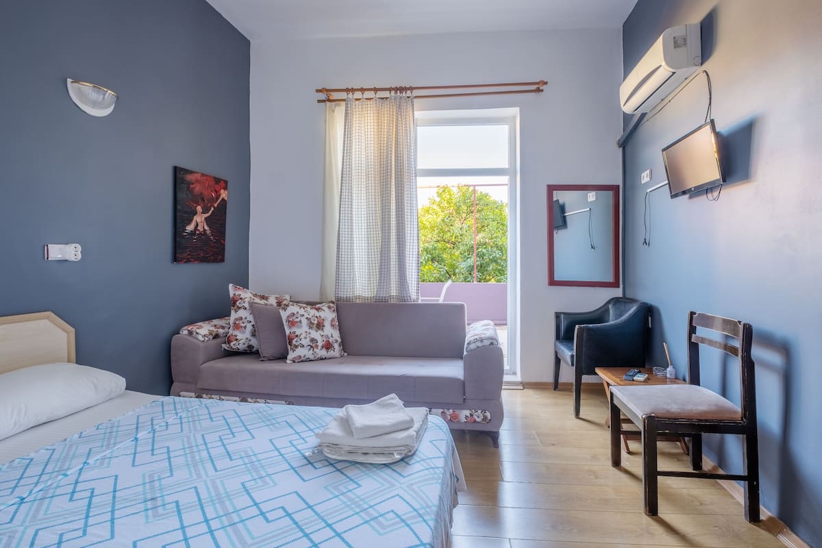 Une chambre à coucher avec un lit, un canapé, une chaise, une télévision et une fenêtre avec des rideaux.