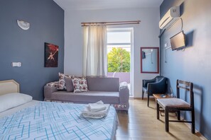 Un dormitorio con cama, sofá, sillón, televisor y ventana con cortinas.