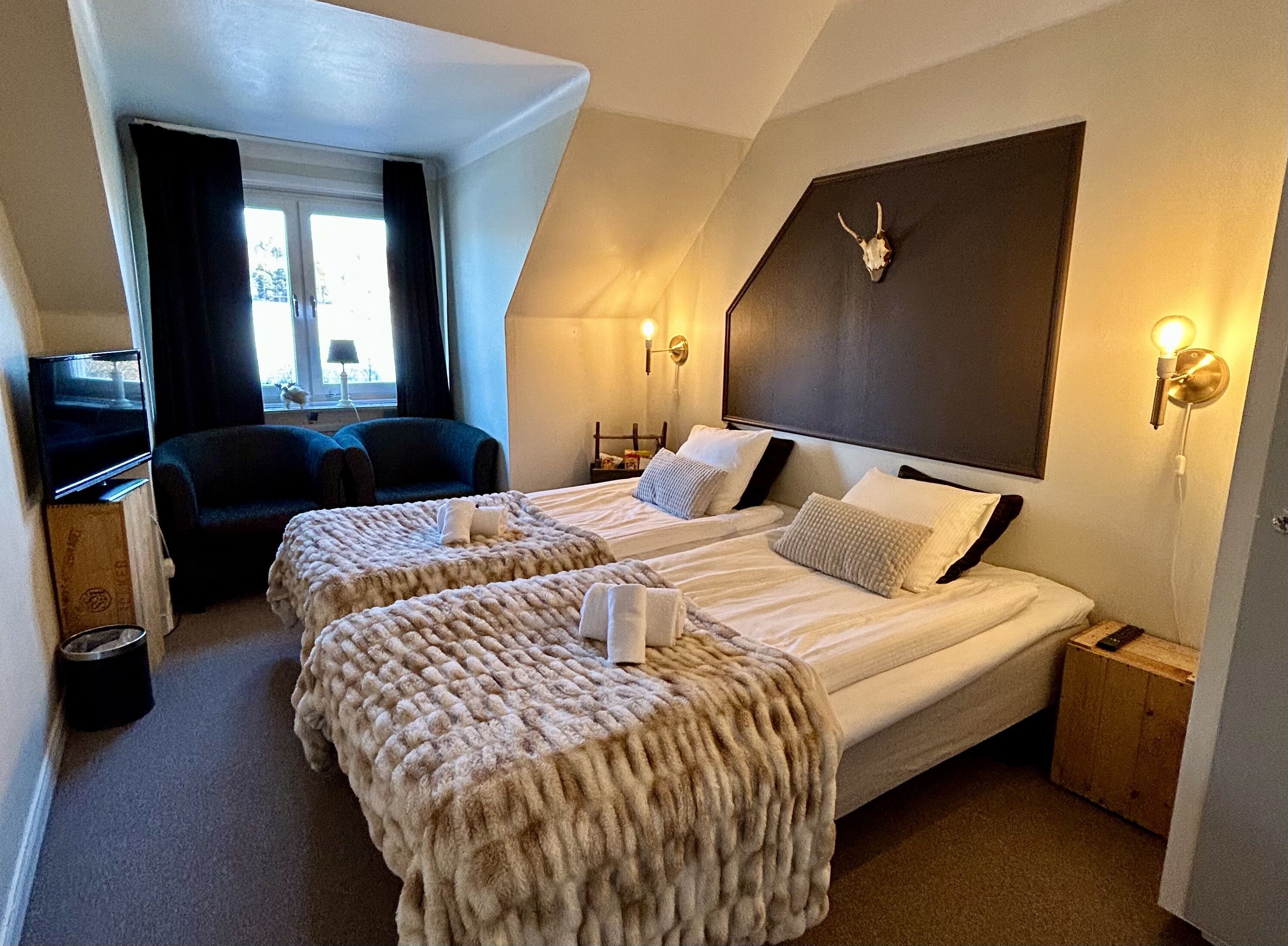 Una habitación de hotel con dos camas, televisión, sofá y ventana con cortinas.