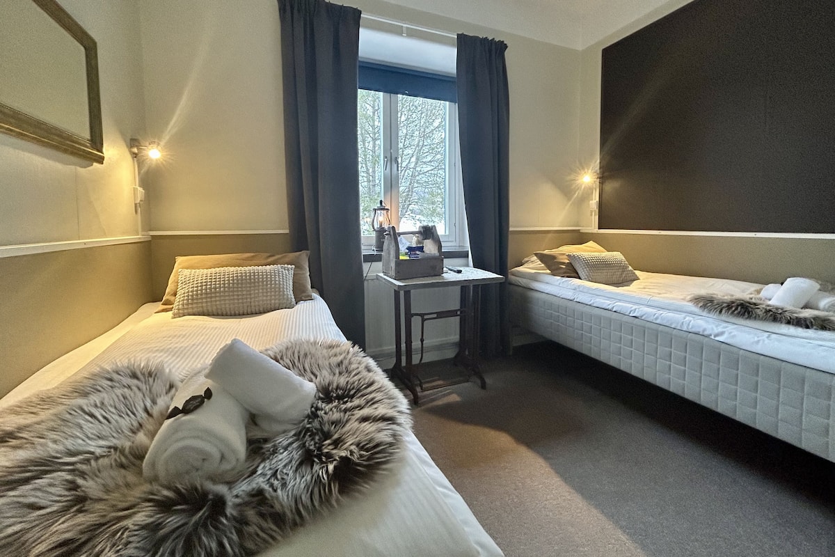 Ett hotellrum med två sängar, ett skrivbord och ett fönster med gardiner.